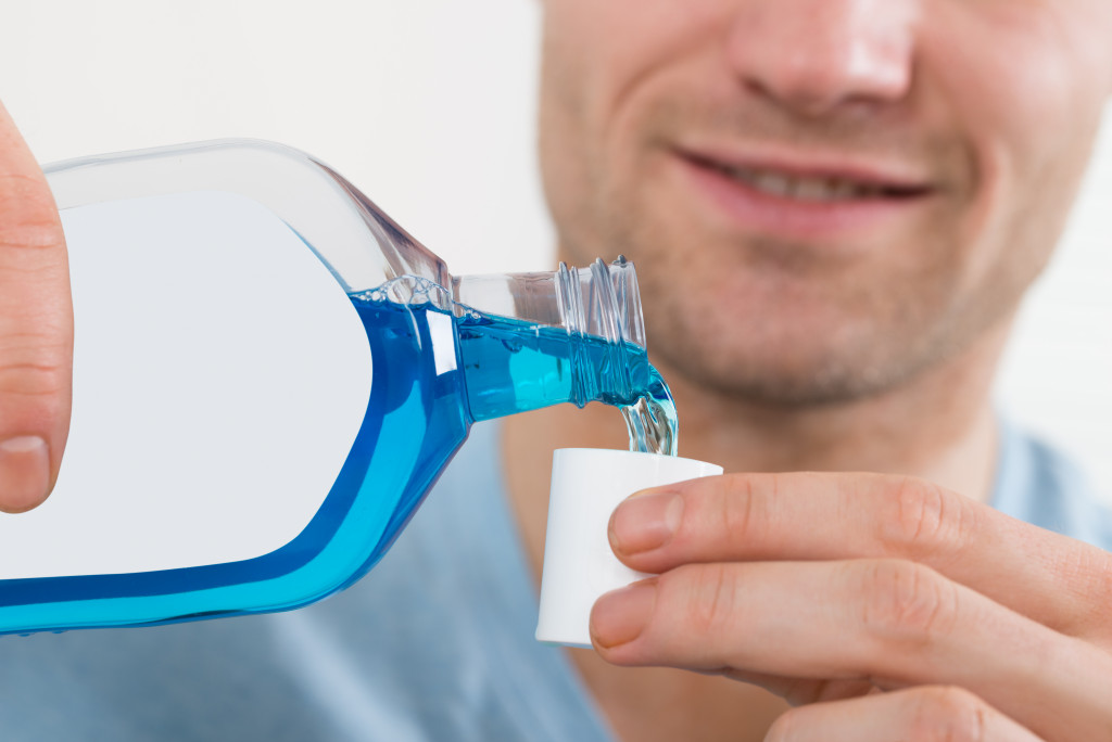man pouring blue colored mouthwash on its cap
