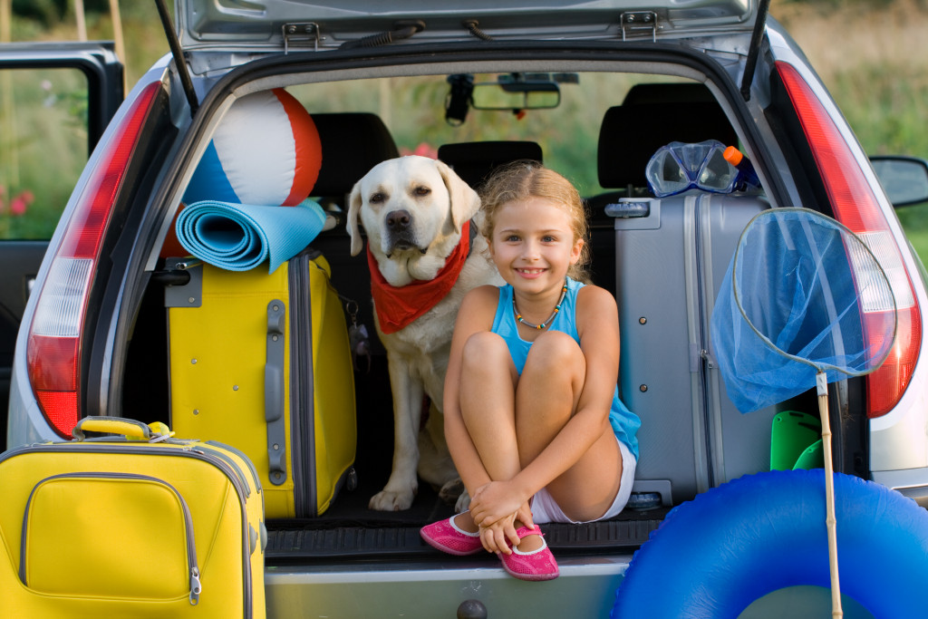 Young girl sitting in the back of a van with her dog while on a family vacation.