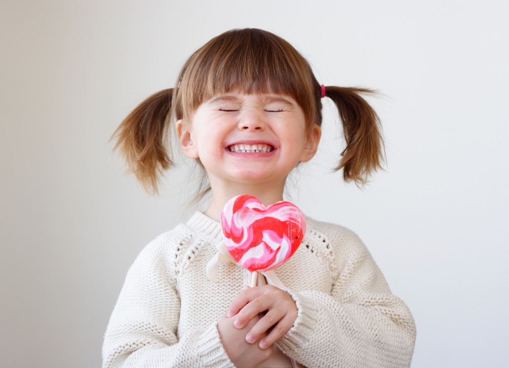 a happy little girl in pigtails holding a big heart shaped lollipop
