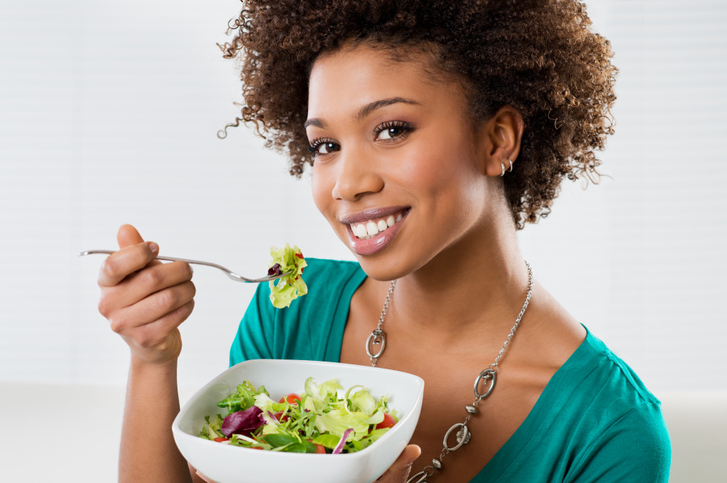 A smiling woman eating a salad wit a fork at home