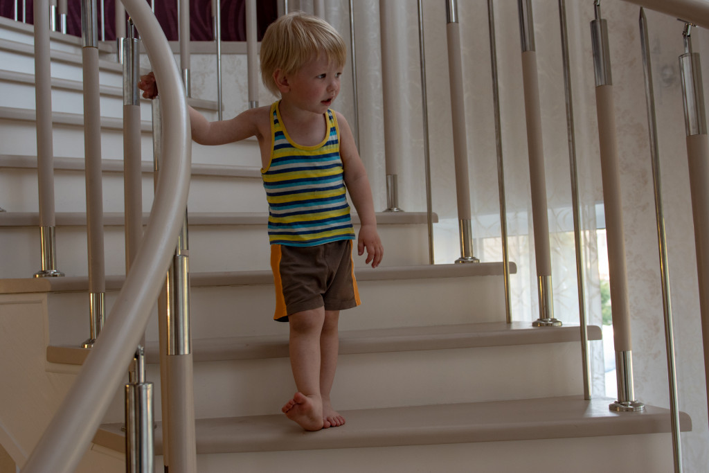 A little boy going down the stairs while holding on a handrail