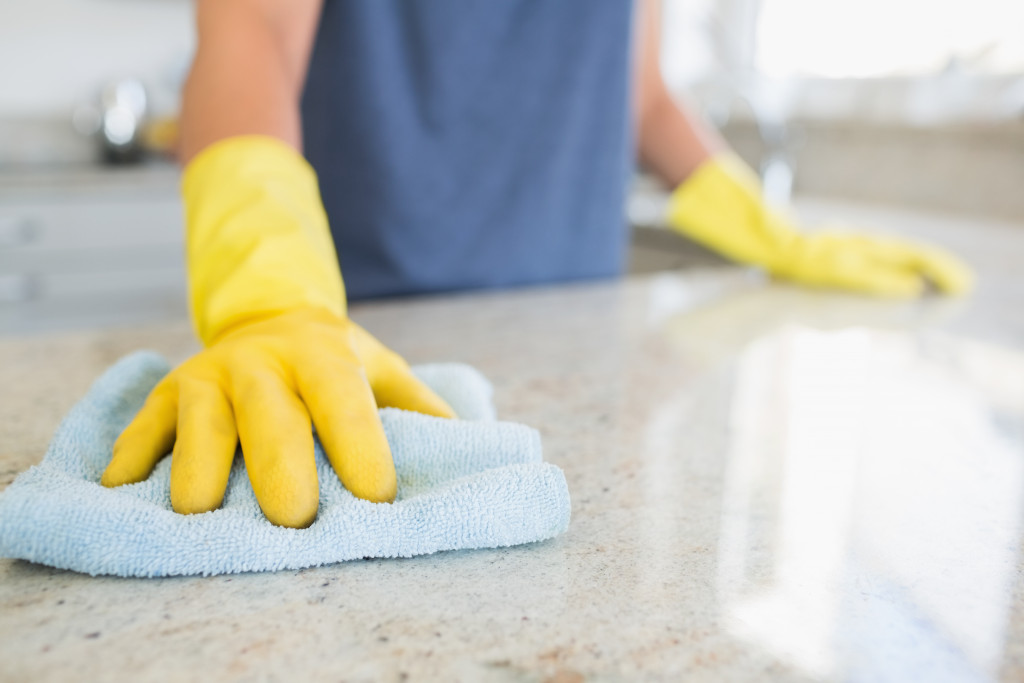 A person wearing yellow rubber gloves wiping a kitchen counter with a cloth