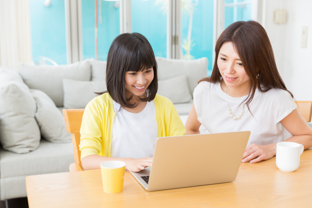 a young pre-teen girl sitting beside her mother while using the laptop