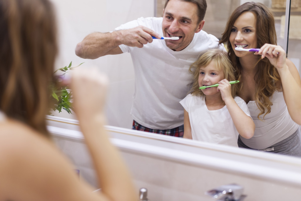 Parents teaching their daughter how to brush her teeth properly in the bathroom.