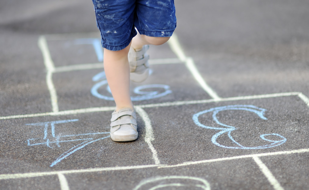 A child playing hopscotch on a concrete road with chalk drawings