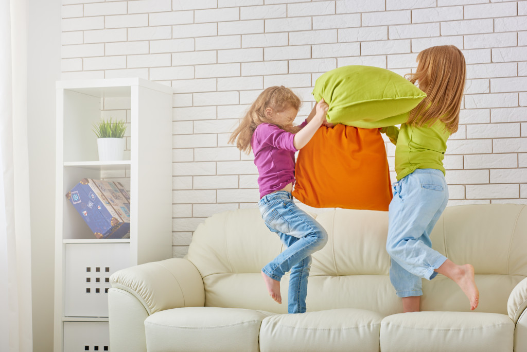 Two young girls playing with pillows on a living room couch