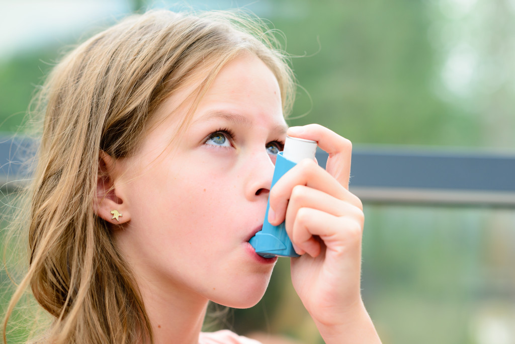young girl using asthma inhaler outdoors