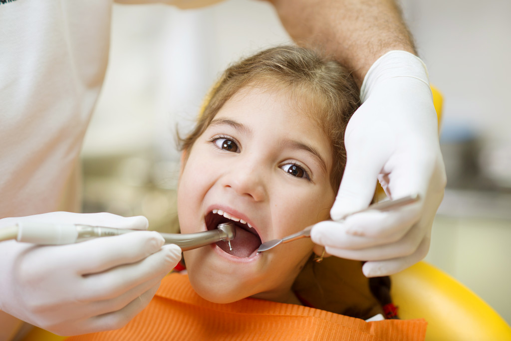 young girl getting teeth checked by dentist wearing gloves