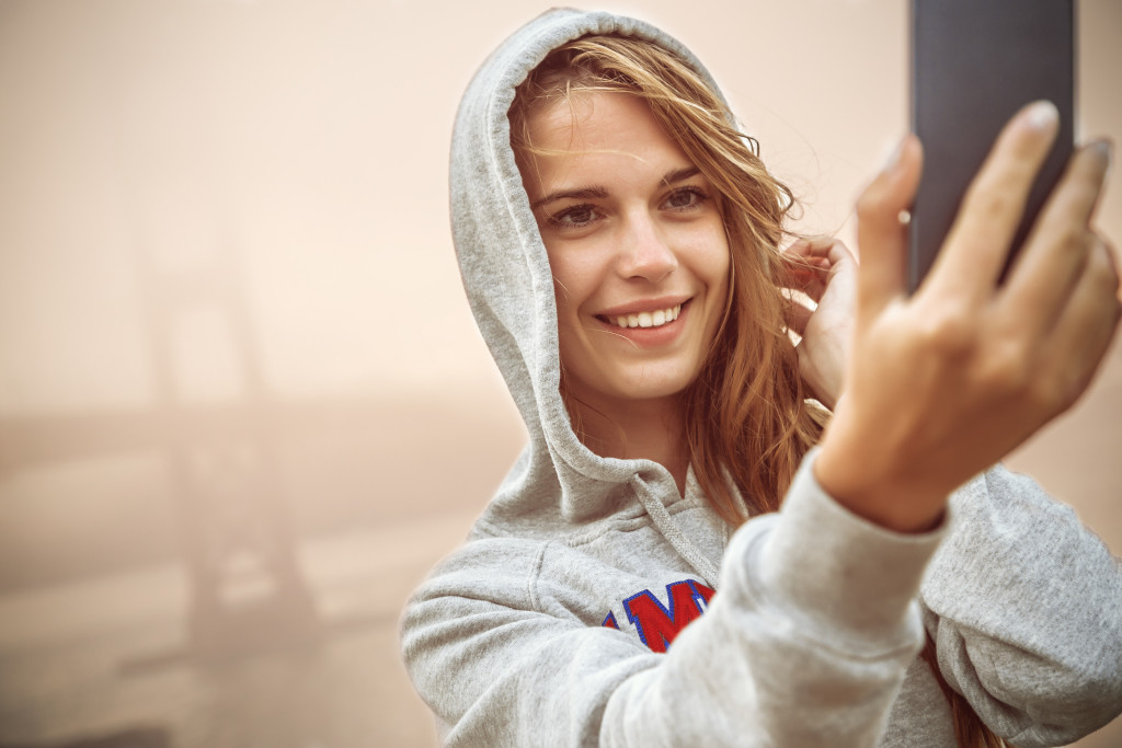 Young adult smiling while taking selfie with a fog-covered bridge behind her.